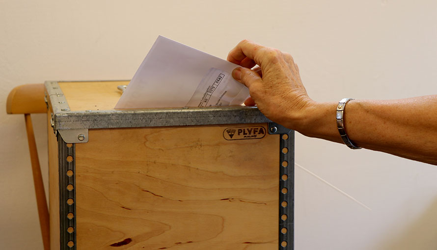 Hand som lägger en röstsedel i en valurna.