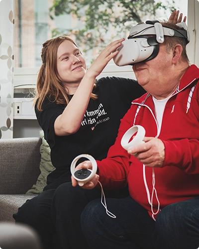 Personal från Träffpunkt Simonsland rättar till ett par VR-glasögon på en äldre man.
