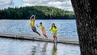 Tre barn hoppar i vattnet från en brygga.