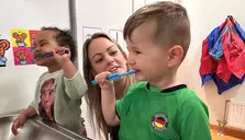 Två barn som borstar tänderna och en pedagog