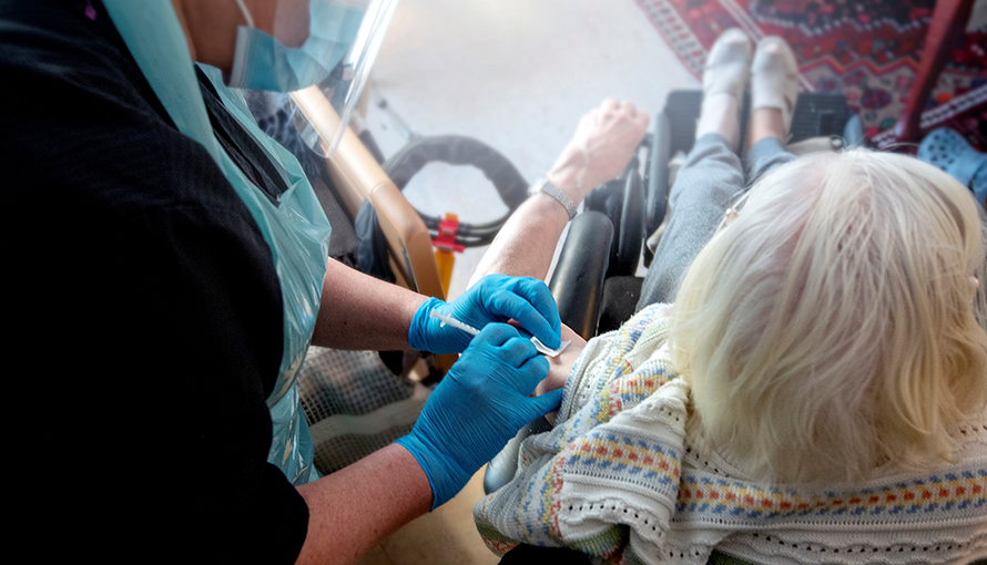 En sjuksköterska vaccinerar en kvinna som sitter i rullstol.
