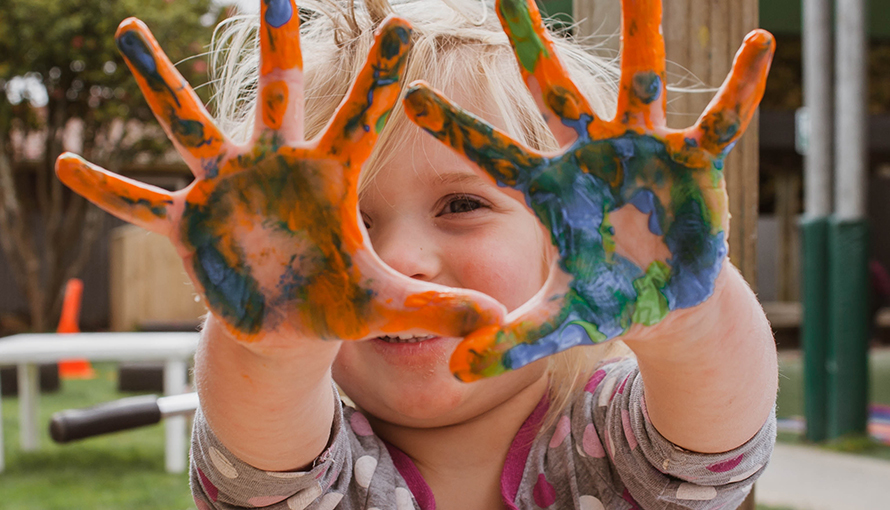 Ett barn håller upp sina händer som är kladdiga med målarfärg