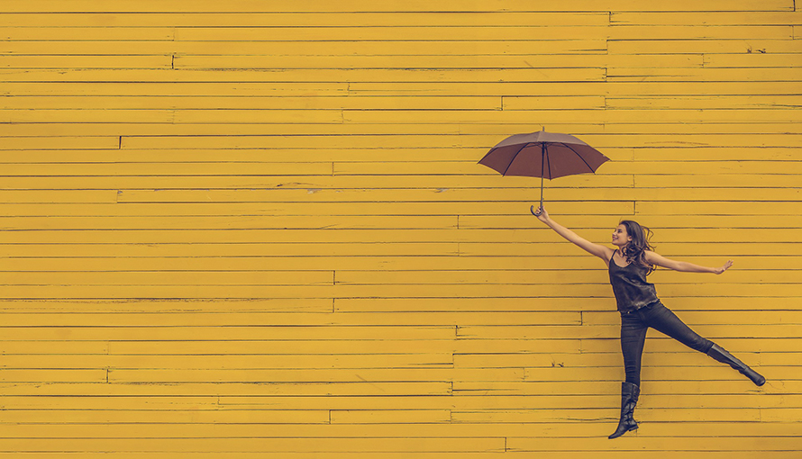 En tjejer med paraply emot en gul vägg. 