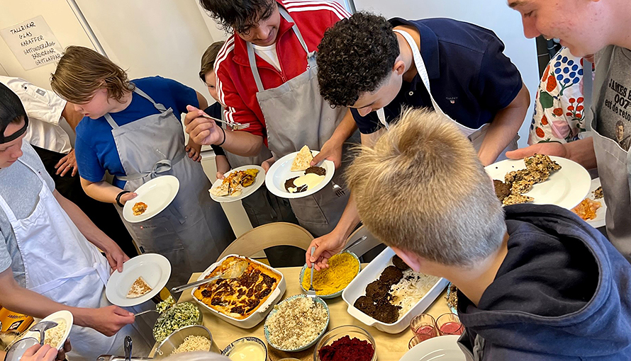 Elever som står med mattallrikar i händerna runt ett bord med mat