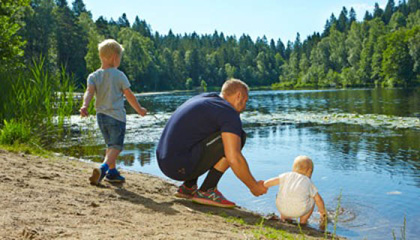 En pappa och två små barn som leker vid stranden av en sjö.