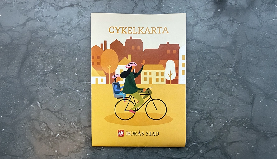 "Cykelkarta" och en illustration av en person som cyklar förbi byggnader. Texten ”BORÅS STAD” syns tydligt.