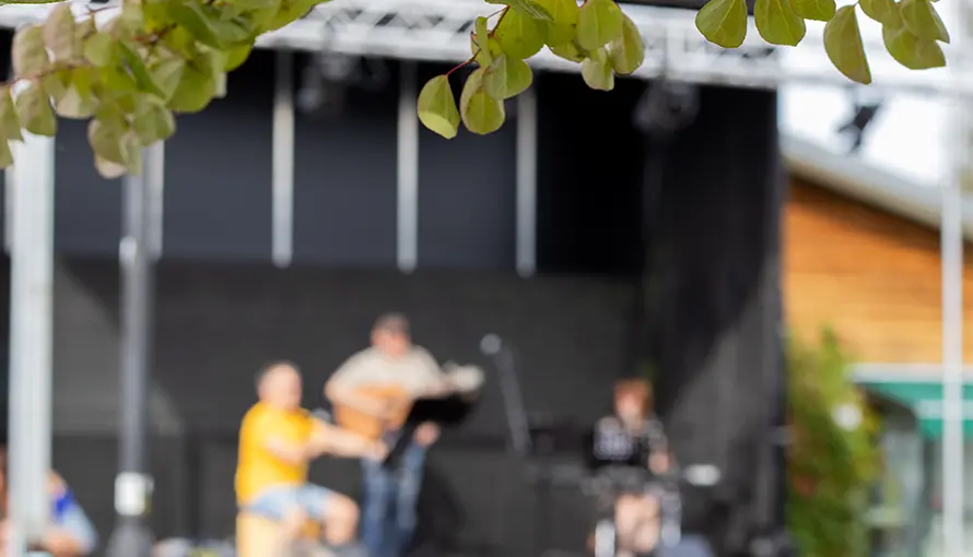 Löv från träd i fokus, i bakgrunden står personer på scen och uppträder