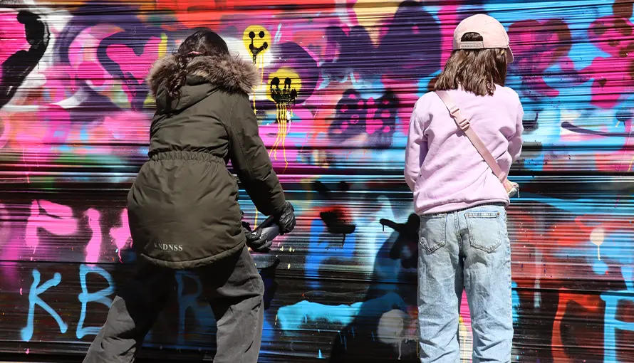 Två barn som målar graffiti på vägg