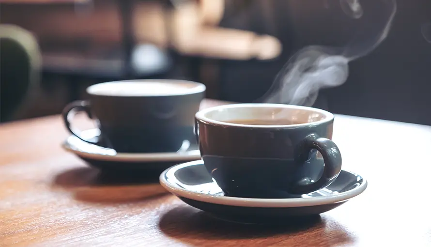 Två svarta kaffekoppar med kaffe i på ett bord av trä