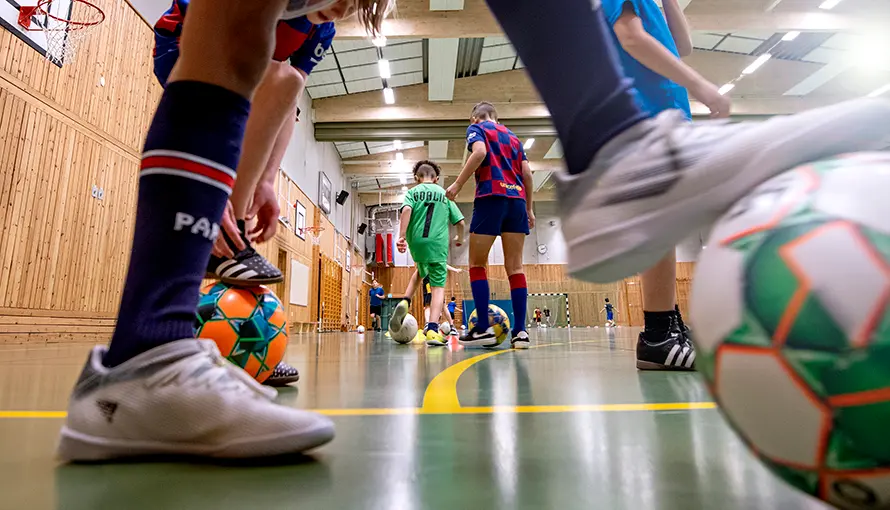 Bilden visar fötter och en fotboll. I bakgrunden spelar barn fotboll.
