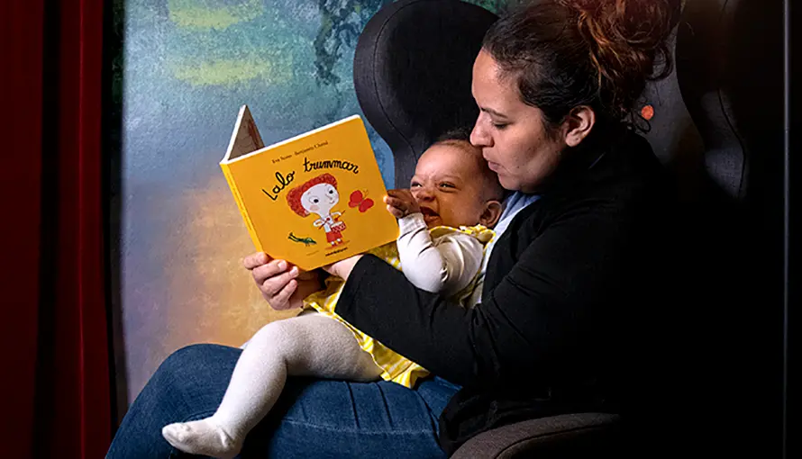 En mamma sitter med sitt barn i knät och läser en bok.