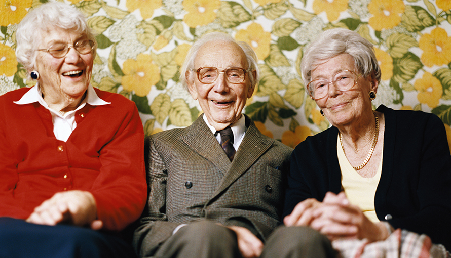 Tre äldre glada personer sitter tillsammans i en soffa