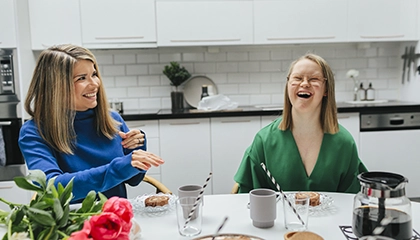 En kvinna och en ung tjej sitter i ett kök. De skrattar och fikar.