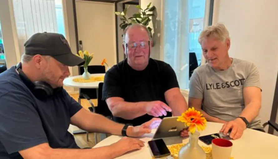 Tre personer sitter runt ett bord med en laptop och tittar på skärmen.
