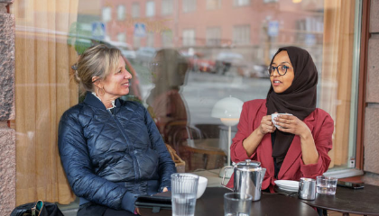 Två kvinnor sitter ute på ett café och pratar.