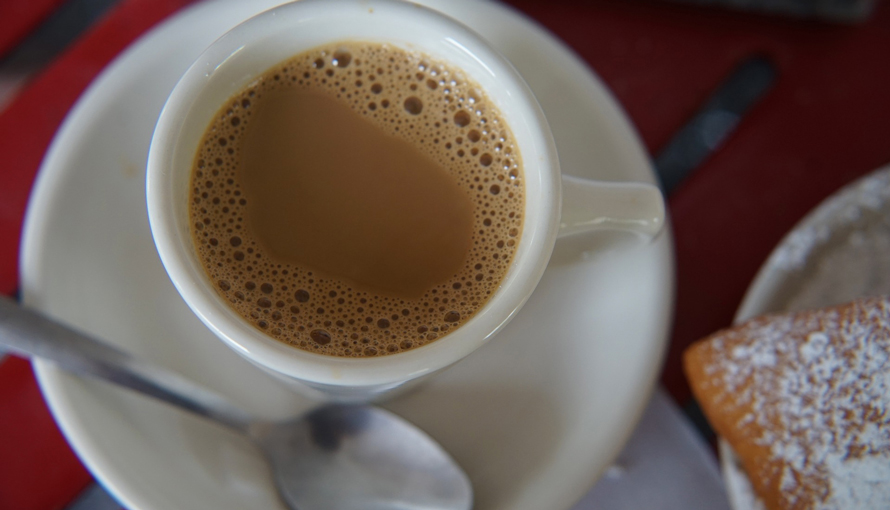 Bilden visar en kopp kaffe med fat och sked, samt en kaka.