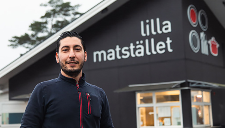 Foto på Bachar Naiem framför byggnaden för restaurangen Lilla matstället. En svart byggnad med loggan i vit text. 