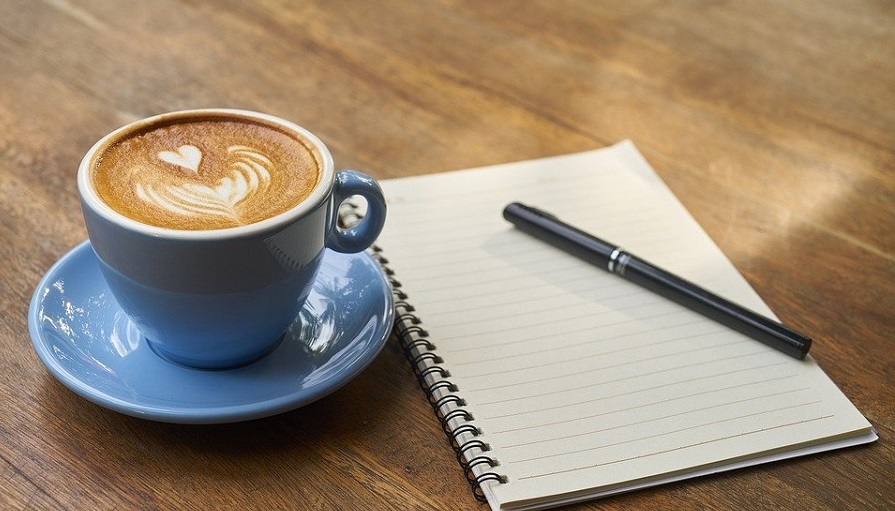 En blå kaffekopp, jämte kaffekoppen ligger ett anteckningsblock med en penna.