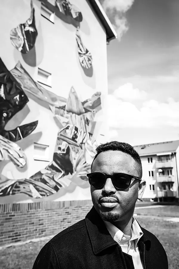Abdirahman står framför ett hus med en muralmålning.