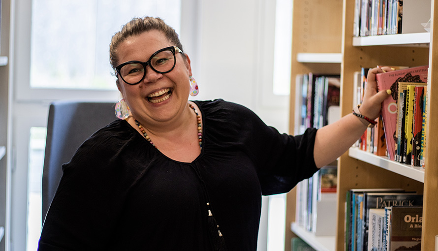 Bild på skrattande kvinna som står vid bokhylla i bibliotek