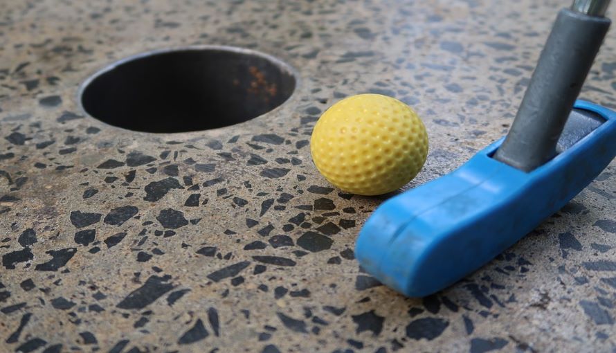 Minigolfklubba som puttar en gul golfboll 