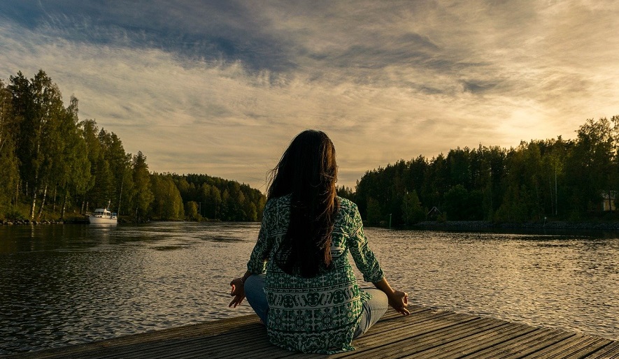 En kvinna som sitter på en brygga vid en sjö och mediterar.