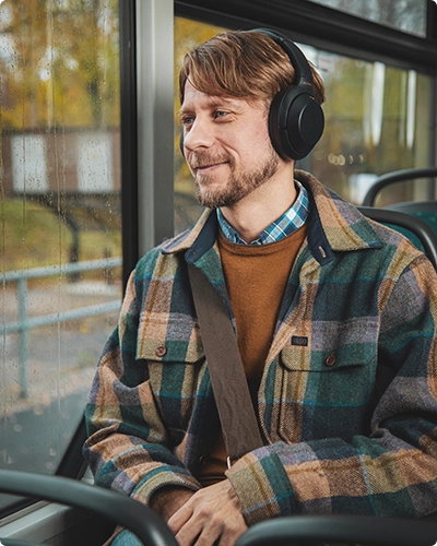 En man som åker buss. Han har hörlurar på sig och ser glad ut.