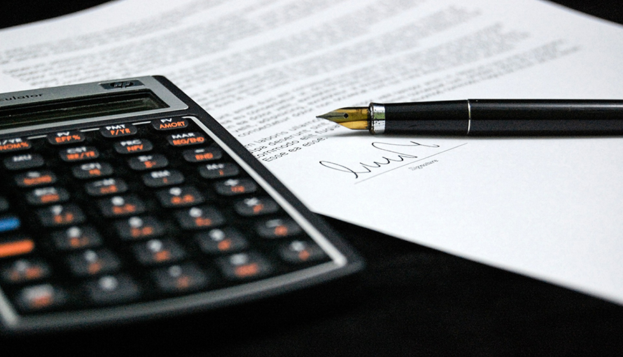En miniräknare och ett signerat avtal på ett svart skrivbord. 