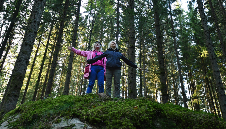 Foto på två kvinnor som står på en stor sten och tittar ut över skogen