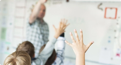 Lärare vid whiteboard, elever räcker upp händer