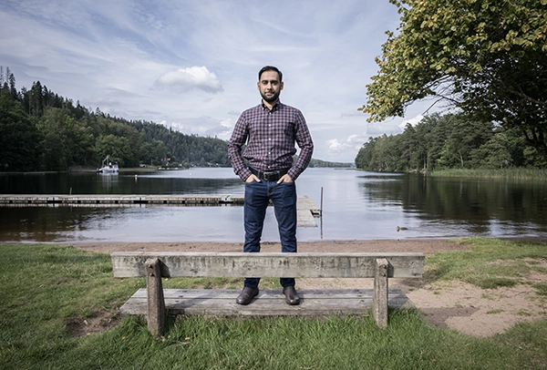 Taimur Khan står på en parkbänk med en sjö bakom sig.