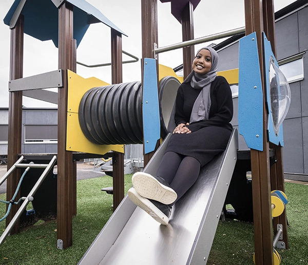 Rumesa Hamed sitter i en rutschkana på en förskola. Hon ser glad ut. 