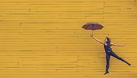 En tjejer med paraply emot en gul vägg. 