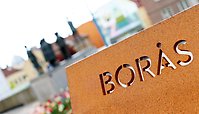 En skylt med texten "Borås". Skulpturen Folktalaren i bakgrunden.