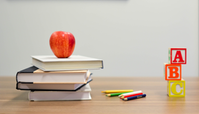 Skolböcker på en bänk tillsammans med ett äpple, pennor och bokstavsklossar