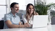 Två personer som sitter framför en datorskärm. De ler. 