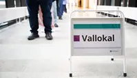 “Vallokal” står på ett metallstöd i en korridor, med personer i bakgrunden.