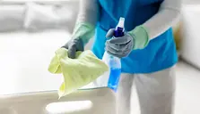 Person rengör med spray och trasa, klädd i blått.