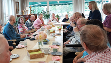 En grupp äldre personer sitter runt ett bord med kaffe och bakverk.