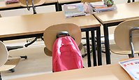 Ett klassrum med en ryggsäck hängande på en stol. 
