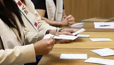 Händer hanterar mottagande ab röster vid ett bord. Ett bälte med texten ”Val” syns.