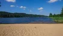 Utsikt över sandstrand, sjö och skog vid Sjöbos badplats
