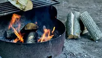 Grillplats med ved som brinner och lite ved som står bredvid