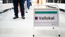 “Vallokal” står på ett metallstöd i en korridor, med personer i bakgrunden.